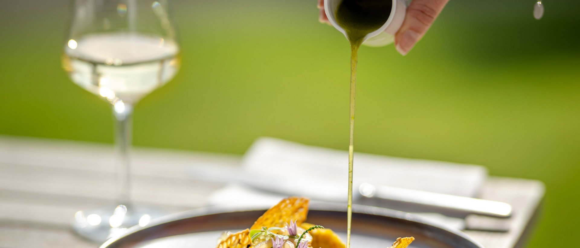 Seezeitlodge : Galerie photos Main verse une sauce verte sur un plat gastronomique artistiquement présenté en extérieur