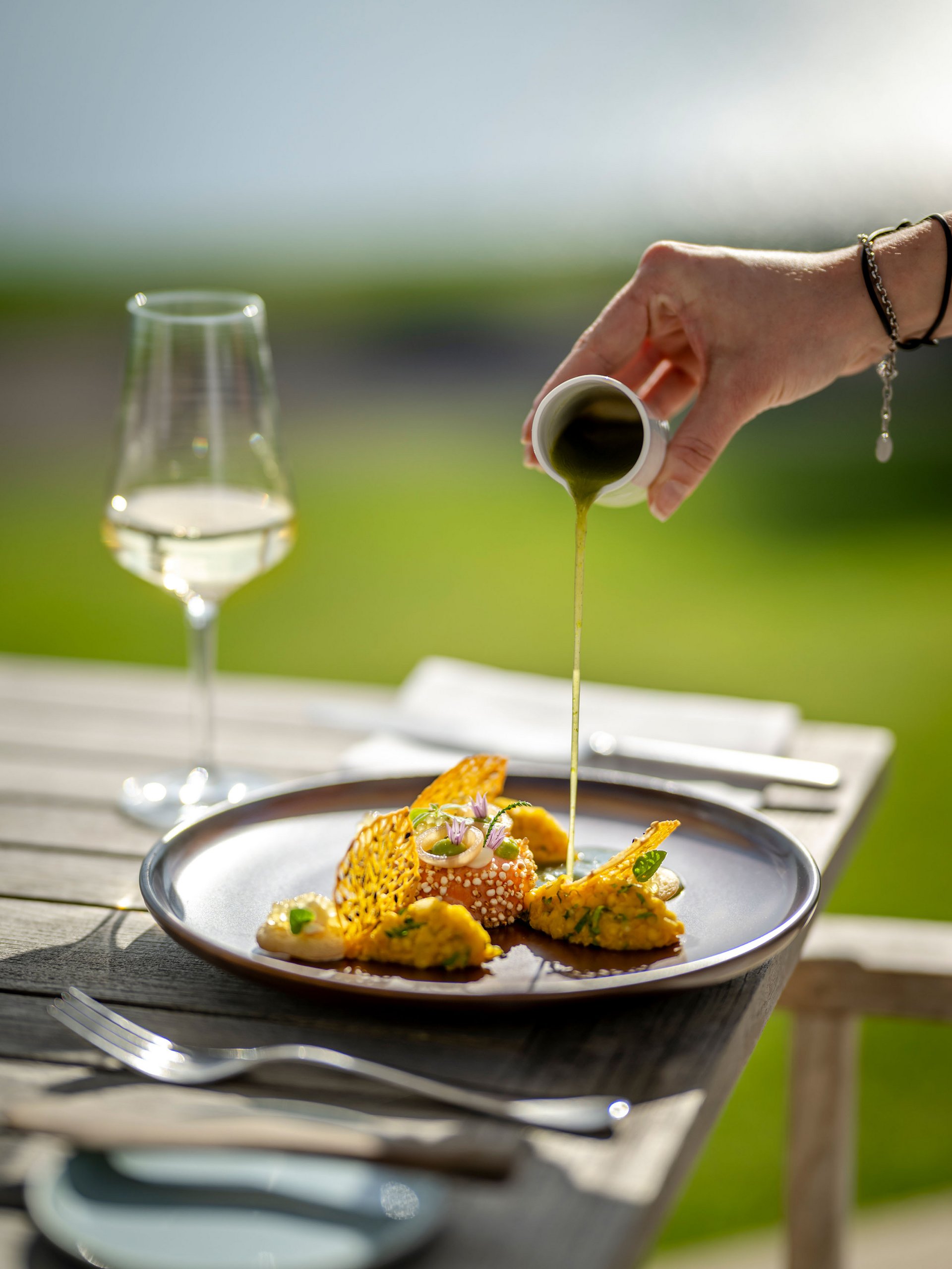 Seezeitlodge : Galerie photos Main verse une sauce verte sur un plat gastronomique artistiquement présenté en extérieur