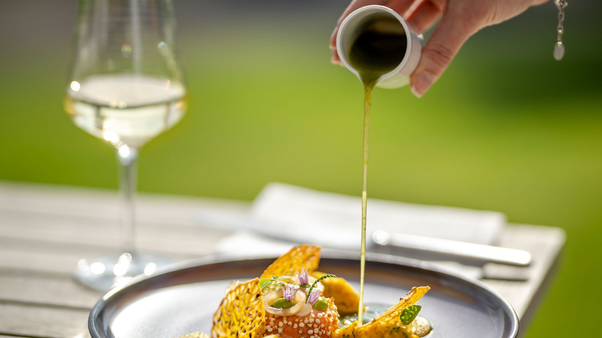 Seezeitlodge : protection des données Main verse une sauce verte sur un plat gastronomique artistiquement présenté en extérieur