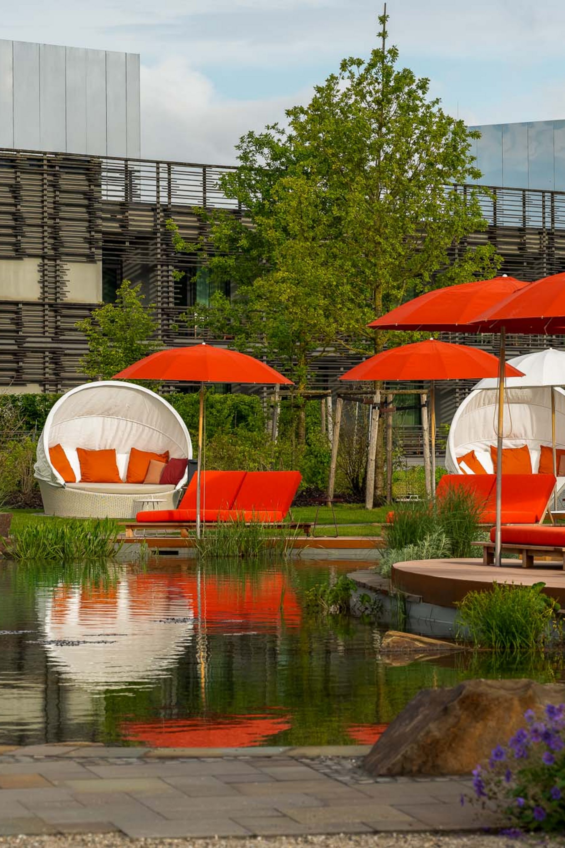 Seezeitlodge: Bildergalerie Outdoor-Liegestühle und Schirme in Rot und Weiß neben einem Teich im Gartenbereich