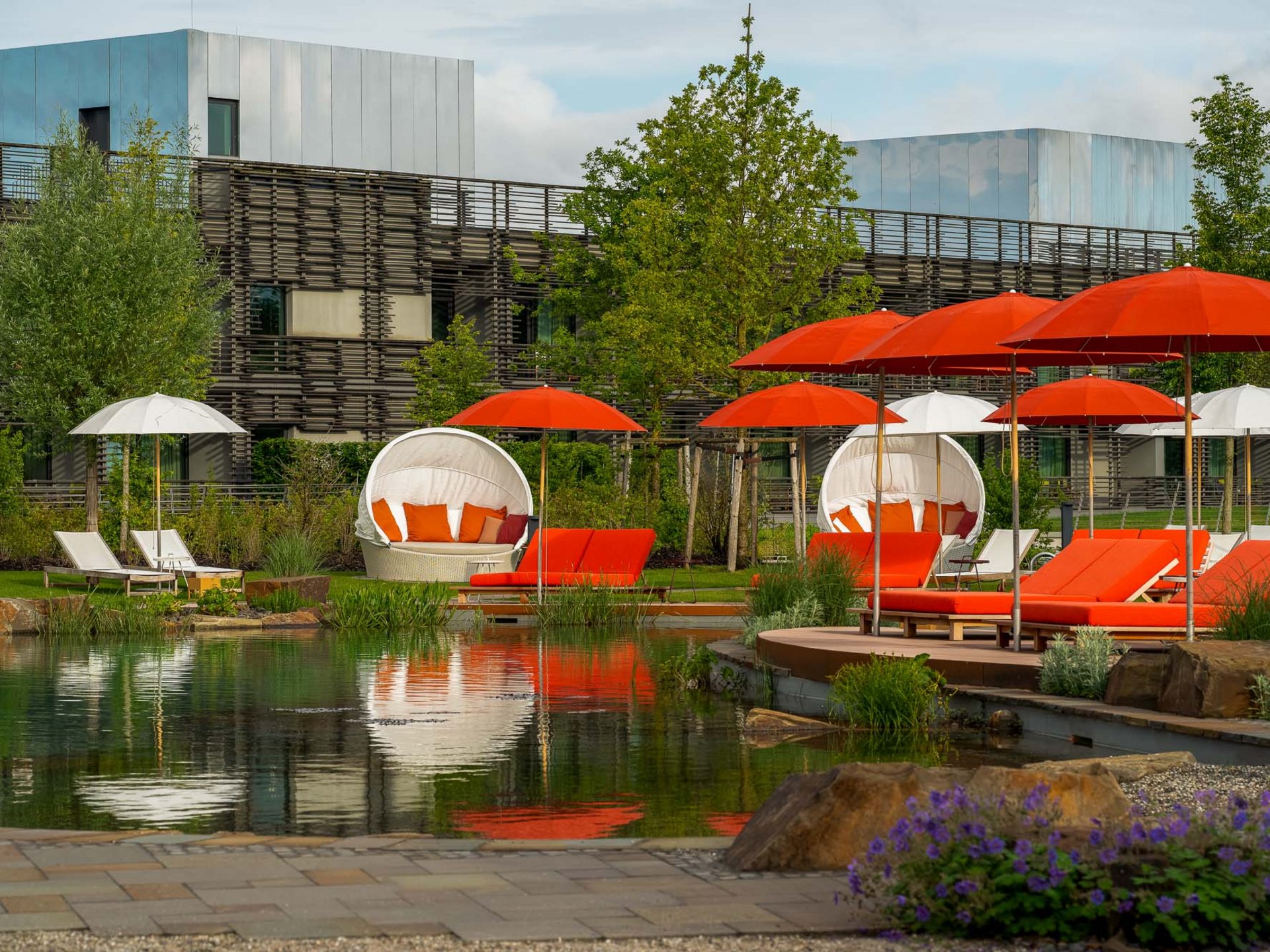 Le Seezeitlodge : votre hôtel au lac de Bostal Chaises longues extérieures avec parasols rouges et blancs au bord d'un étang