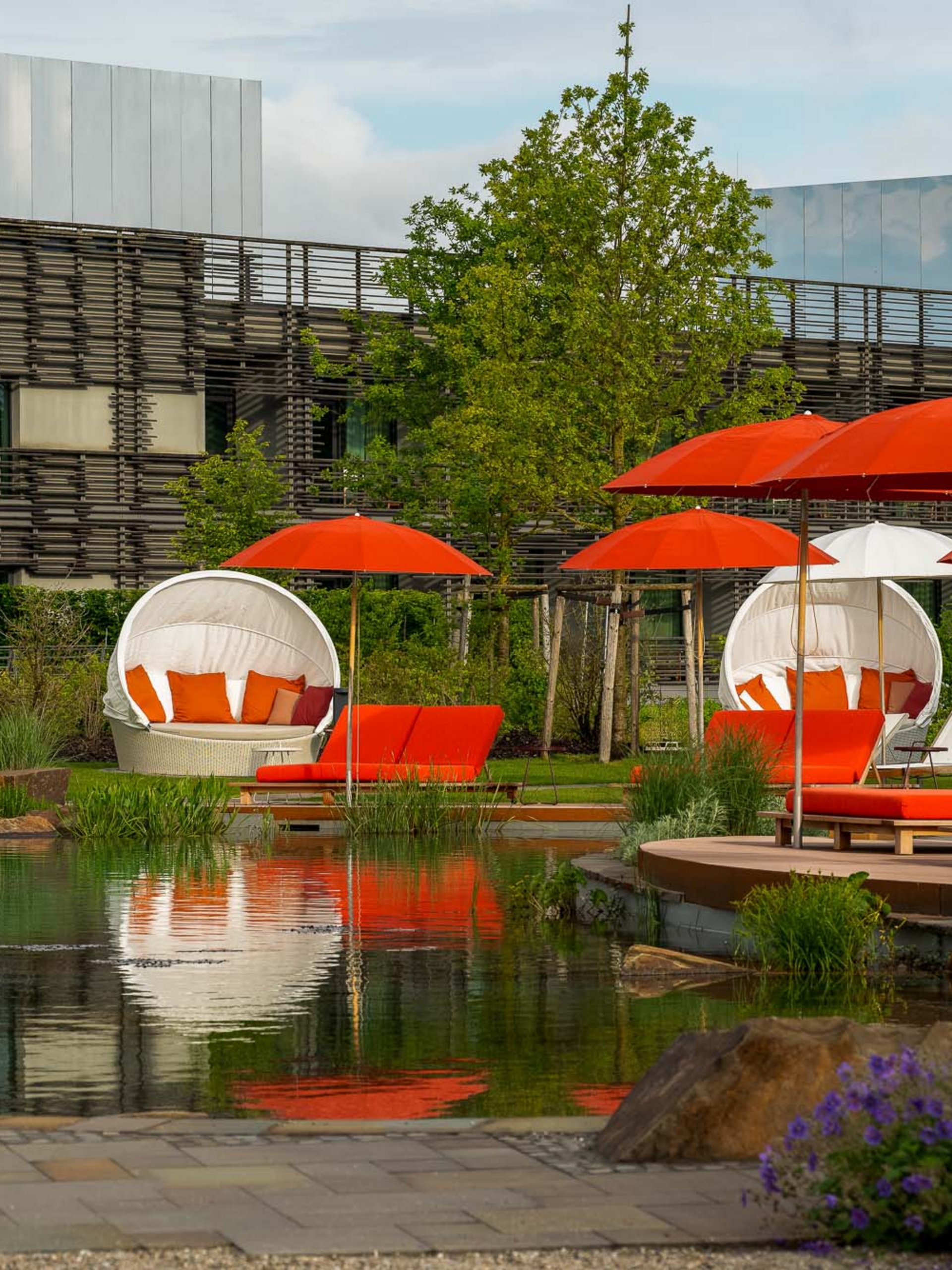 Seezeitlodge : Galerie photos Chaises longues extérieures avec parasols rouges et blancs au bord d'un étang