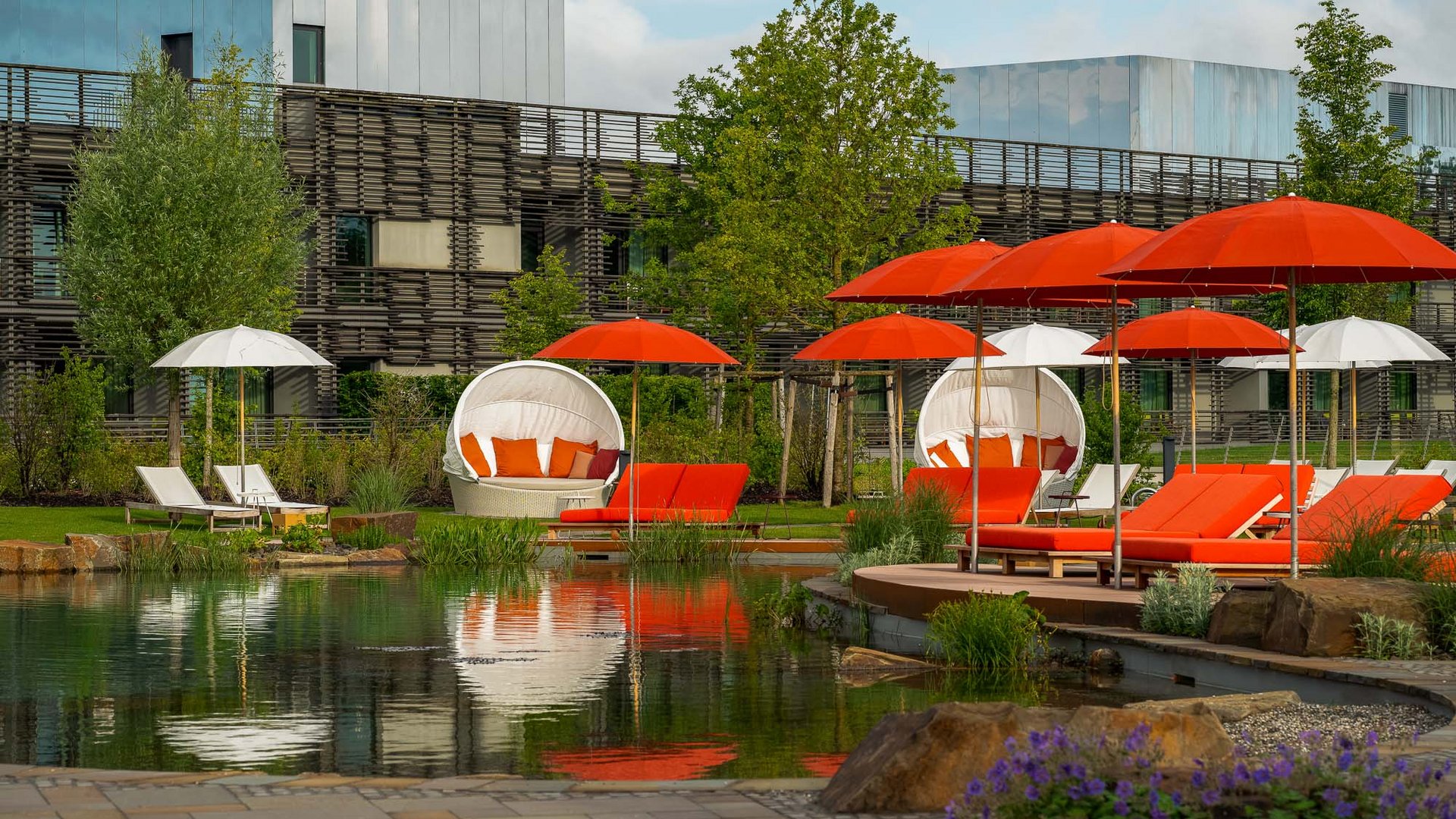 Seezeitlodge : Galerie photos Chaises longues extérieures avec parasols rouges et blancs au bord d'un étang