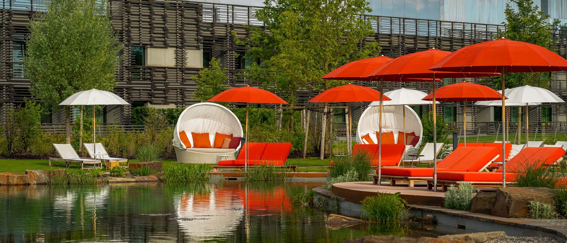 Seezeitlodge: Bildergalerie Outdoor-Liegestühle und Schirme in Rot und Weiß neben einem Teich im Gartenbereich