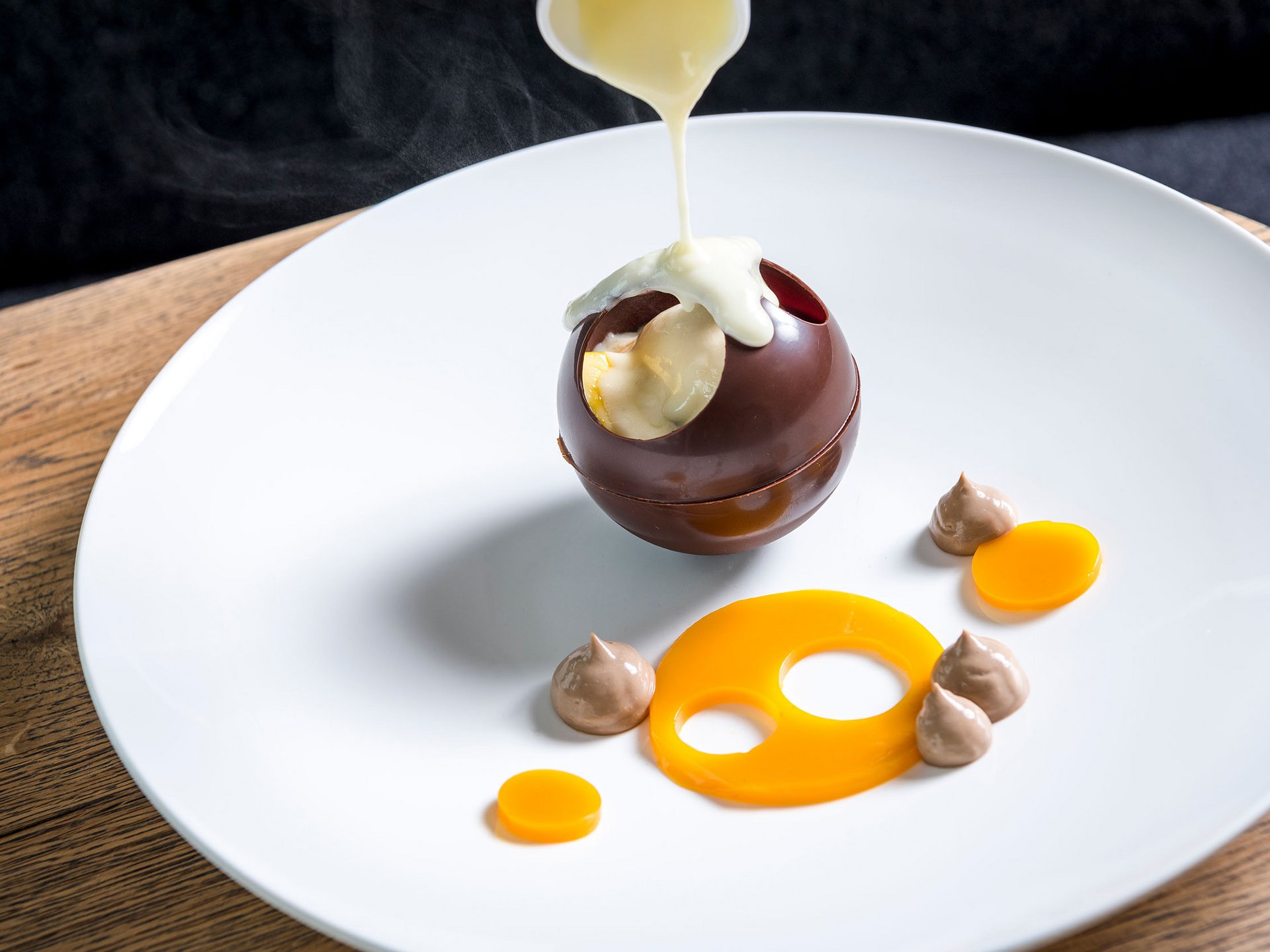 Seezeitlodge: Bildergalerie Heiße Soße wird auf eine hohle Schokoladenkugel auf einem weißen Teller gegossen