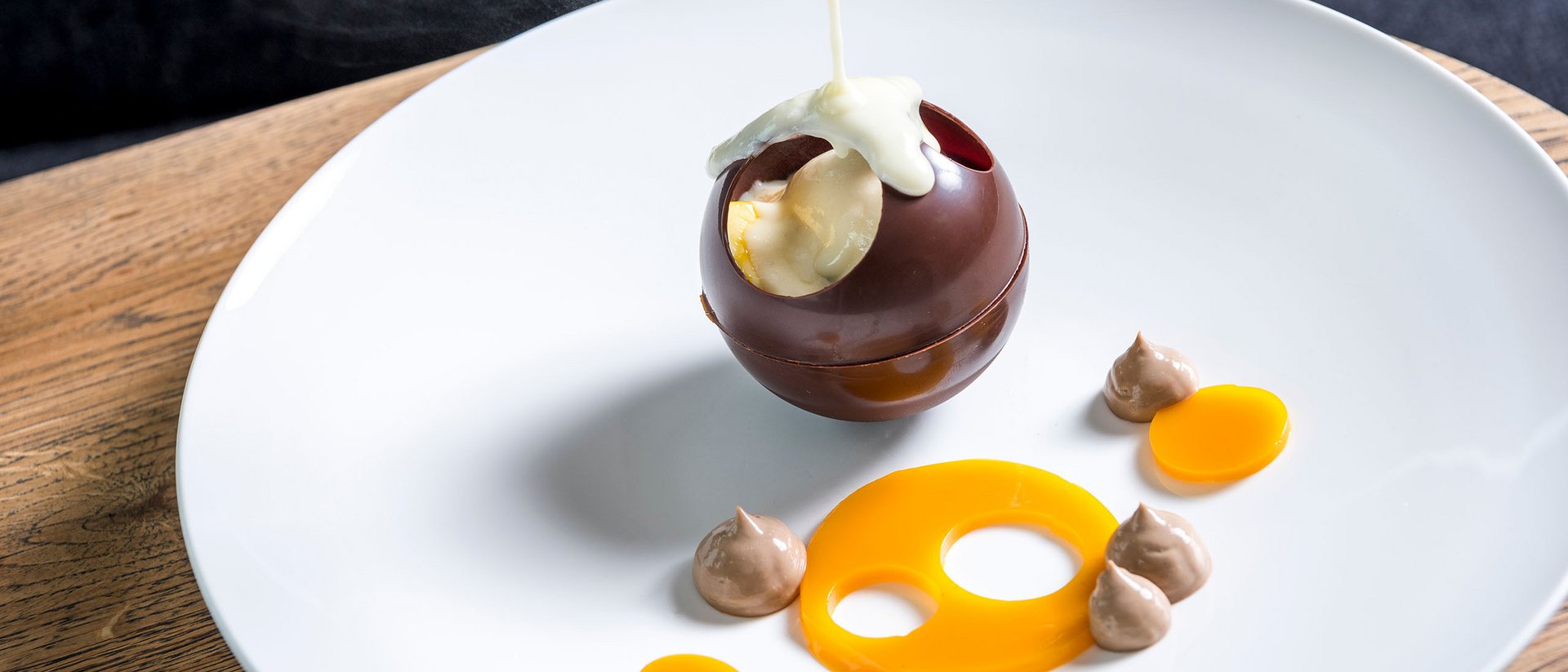 Seezeitlodge: Bildergalerie Heiße Soße wird auf eine hohle Schokoladenkugel auf einem weißen Teller gegossen