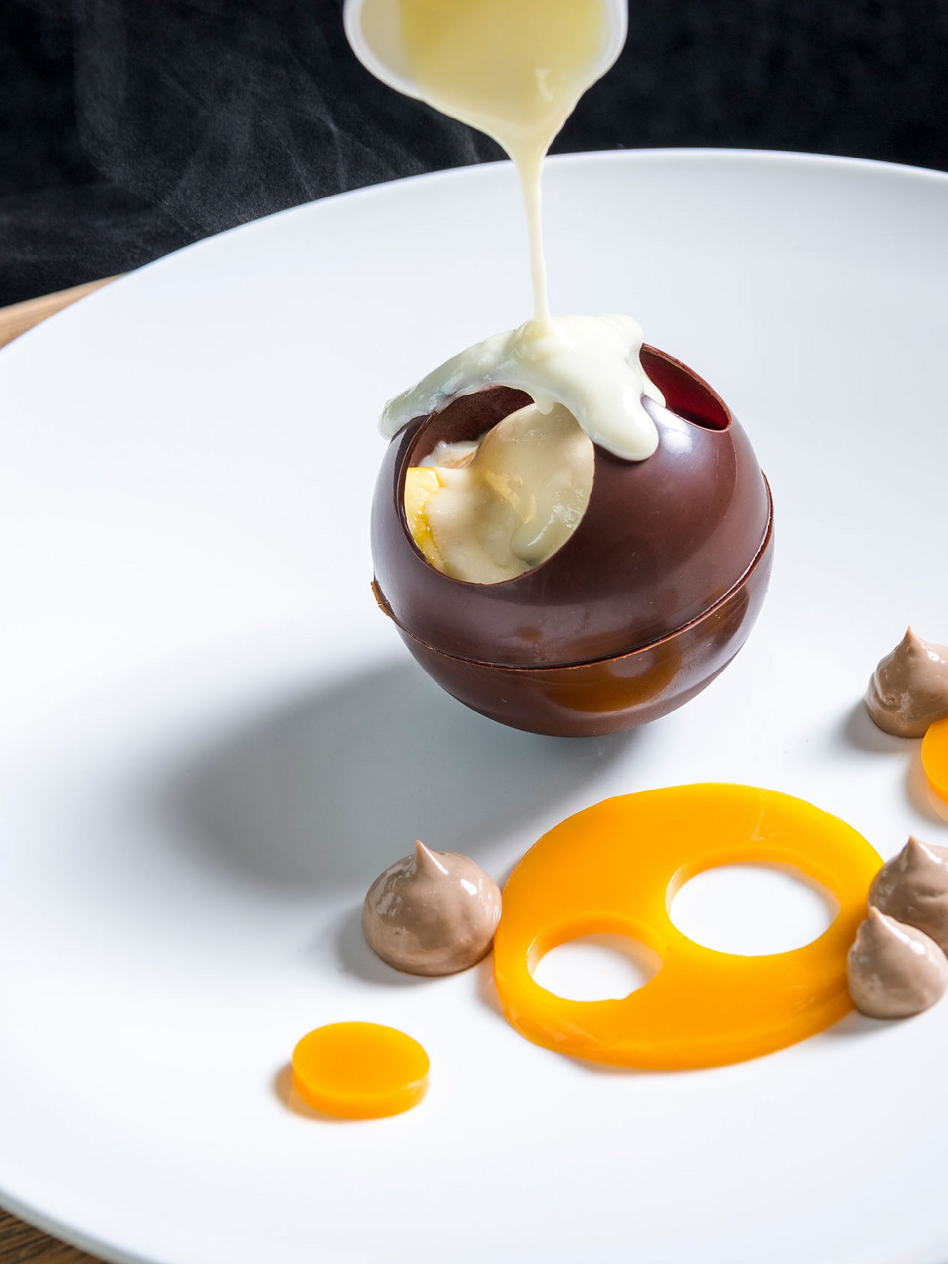 Seezeitlodge: Bildergalerie Heiße Soße wird auf eine hohle Schokoladenkugel auf einem weißen Teller gegossen