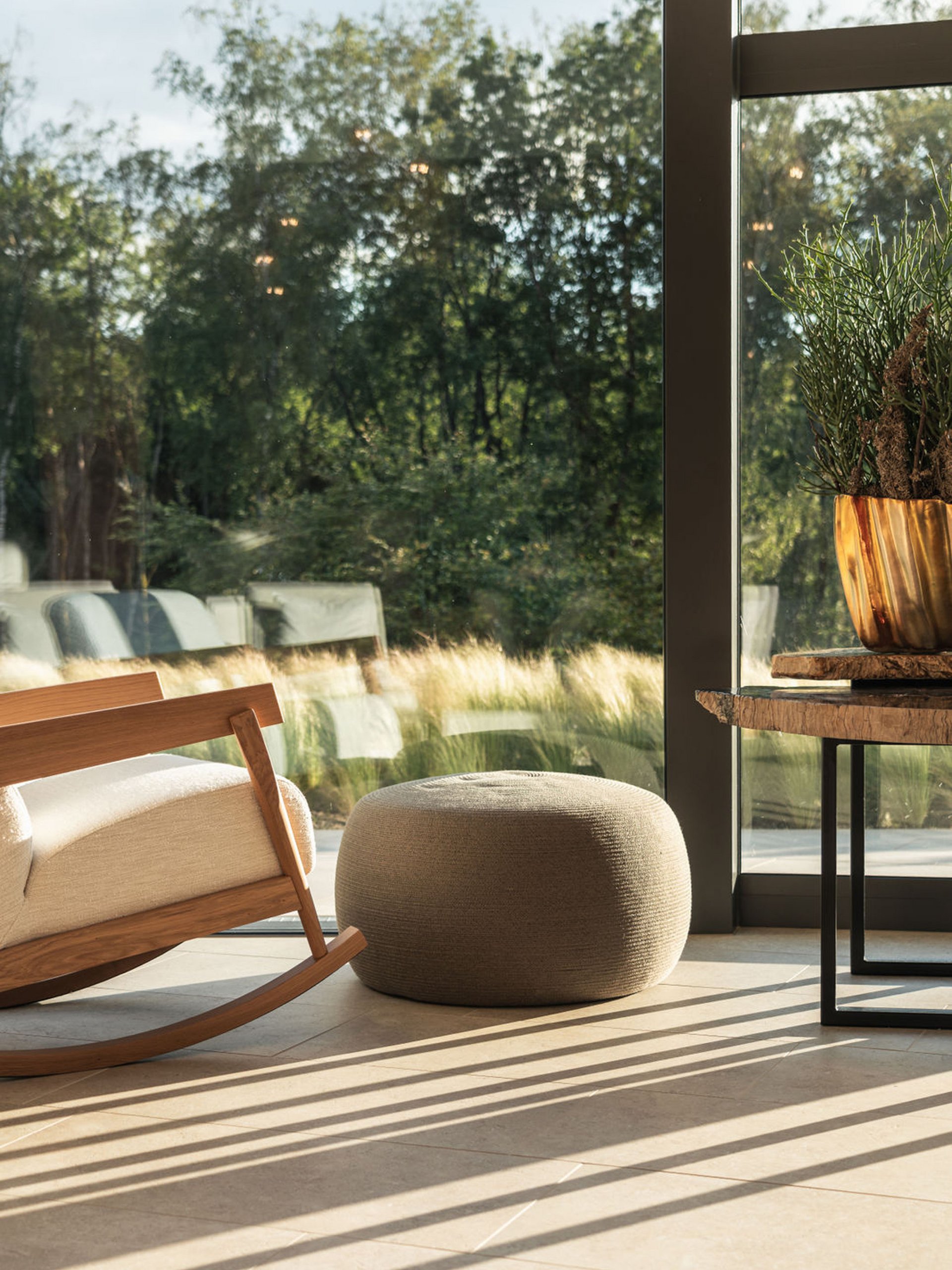 Seezeitlodge: Bildergalerie Gemütlicher Schaukelstuhl, Sitzpouf und Tisch neben großem Fenster mit Blick ins Grüne