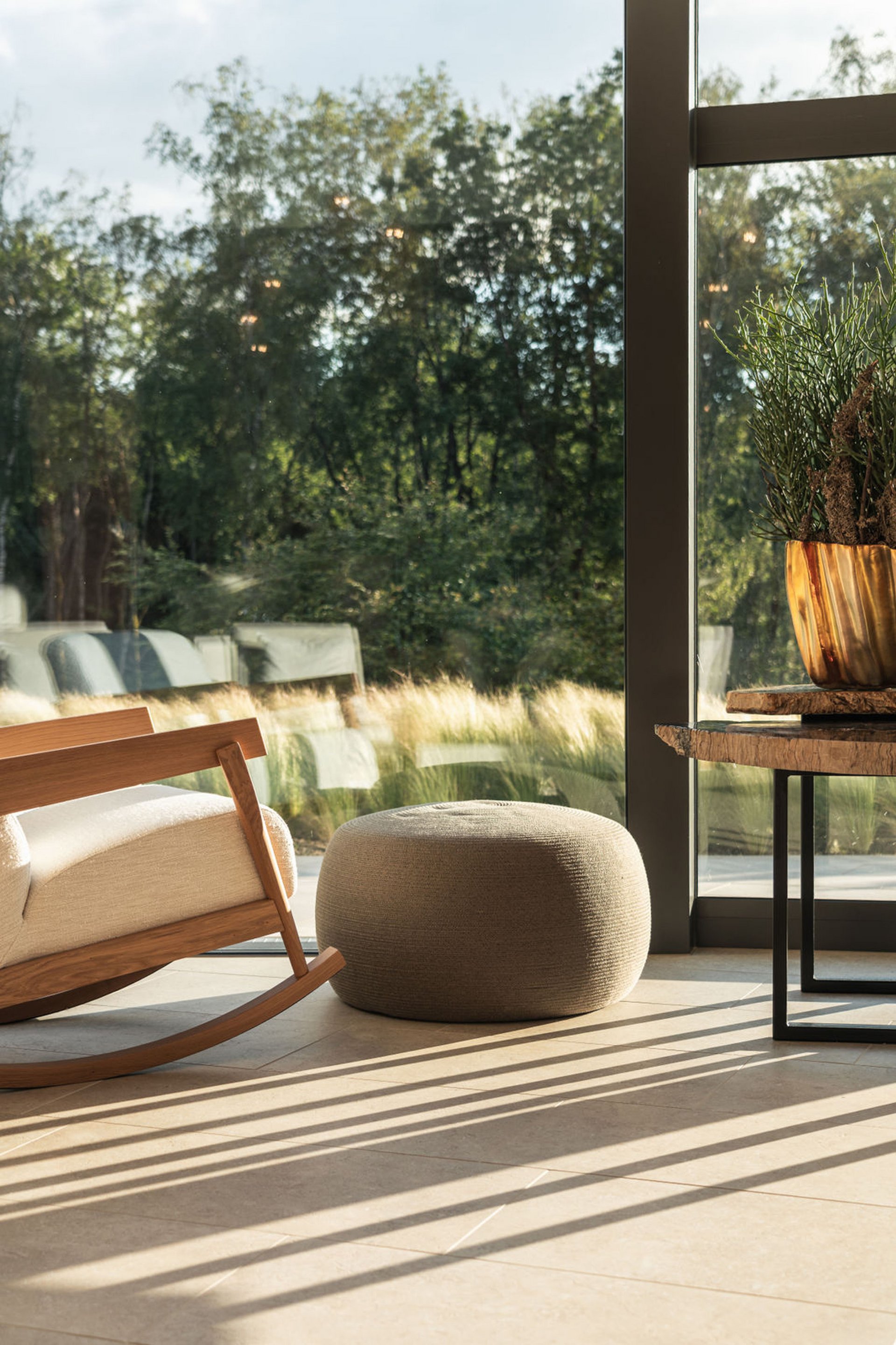 Seezeitlodge: Bildergalerie Gemütlicher Schaukelstuhl, Sitzpouf und Tisch neben großem Fenster mit Blick ins Grüne