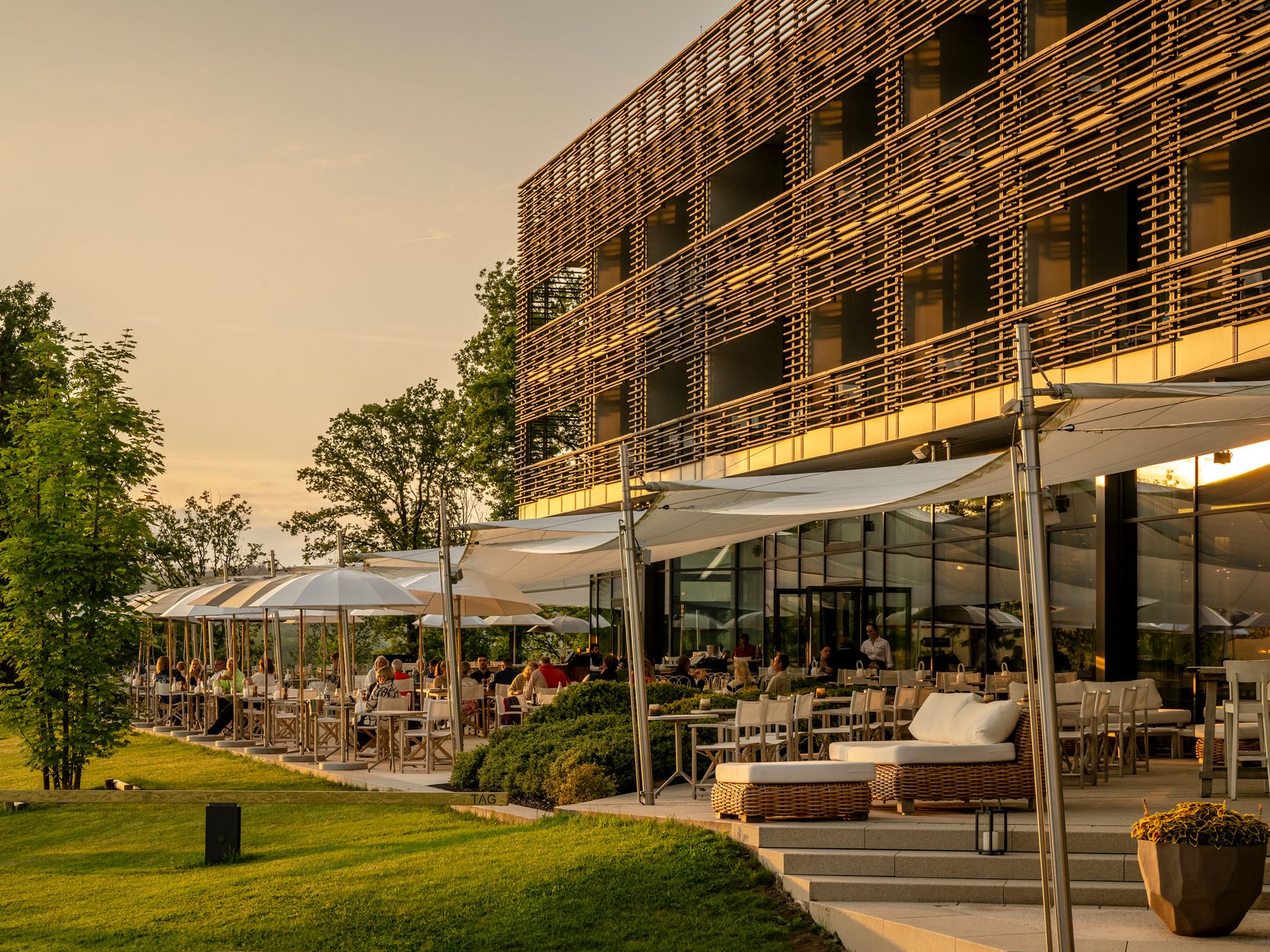 Design hotel Germany: your retreat at Lake Bostalsee Sunny restaurant terrace with guests and modern wooden facade at sunset