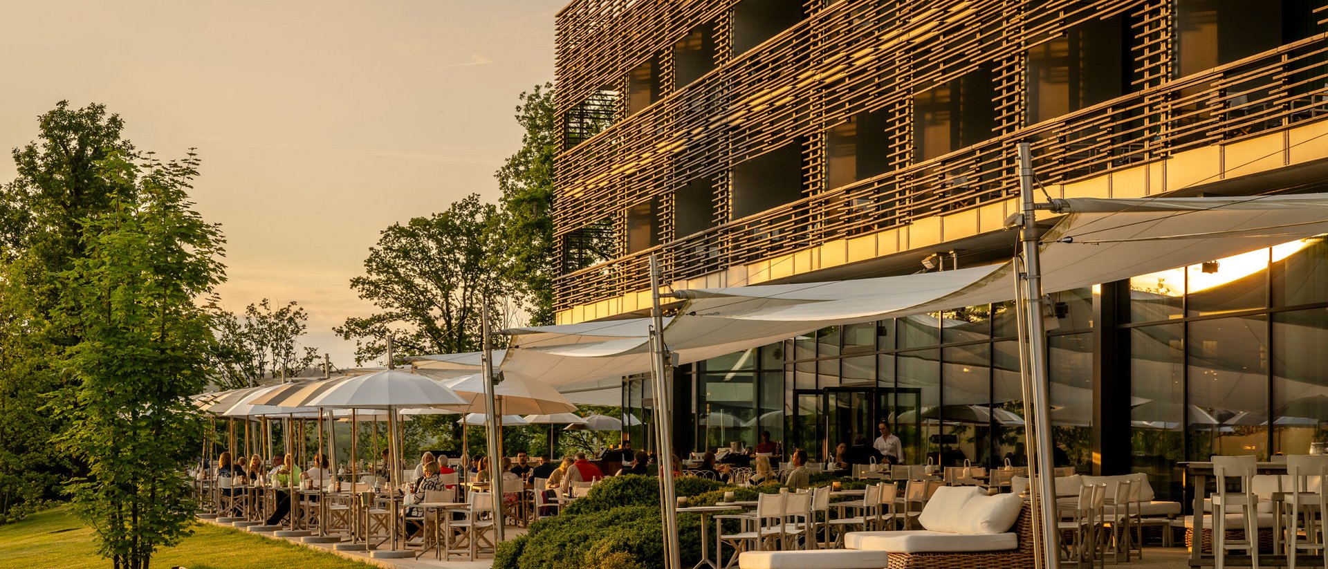 Seezeitlodge : Galerie photos Terrasse ensoleillée d'un restaurant moderne avec des clients au coucher du soleil
