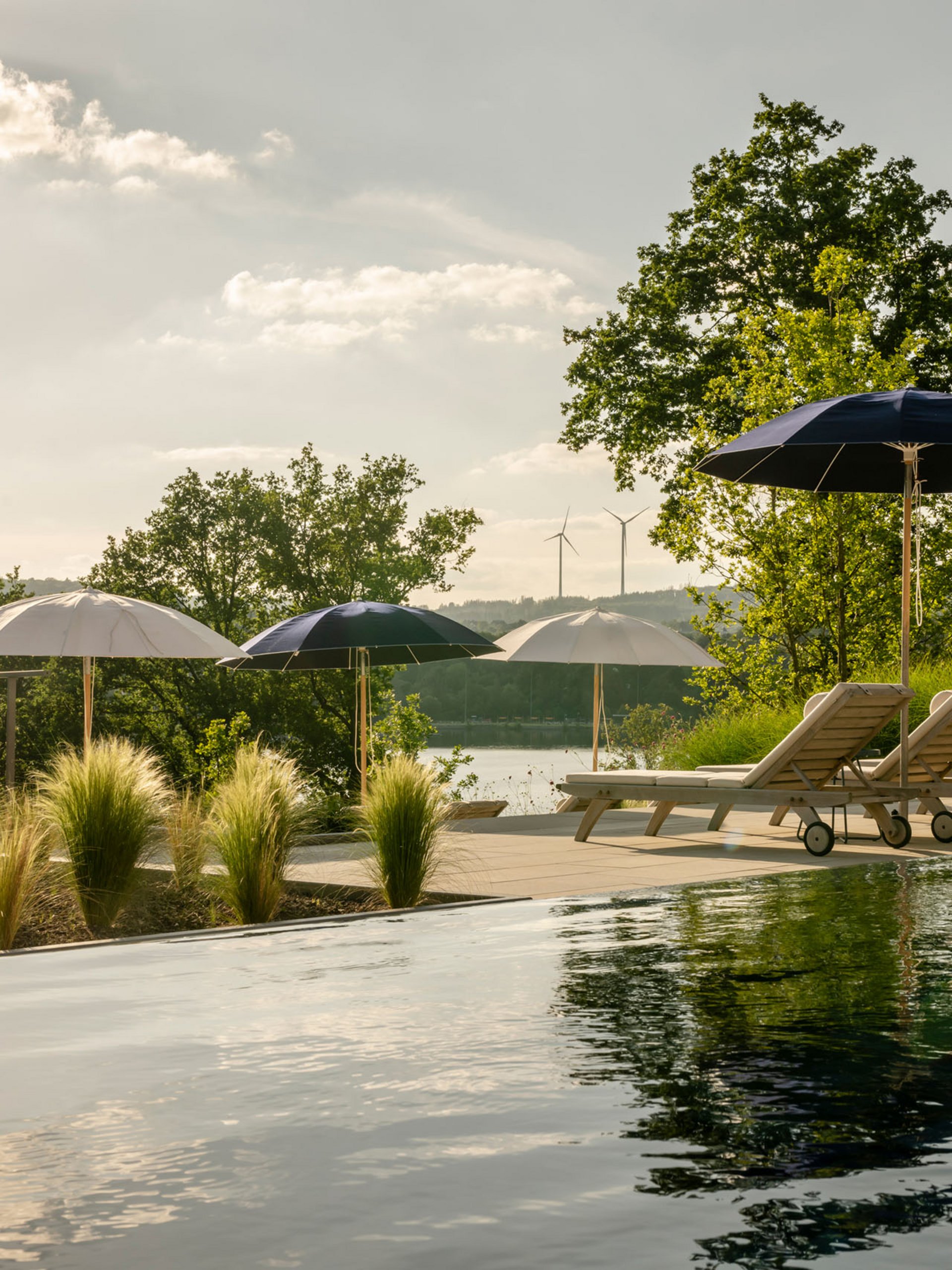 Seezeitlodge : Galerie photos Piscine avec chaises longues et parasols dans un paysage naturel sous la lumière du soleil