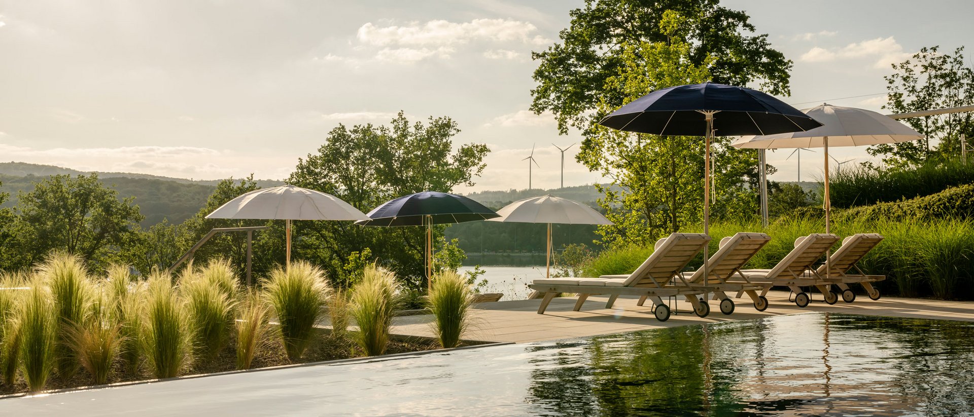 Seezeitlodge : Galerie photos Piscine avec chaises longues et parasols dans un paysage naturel sous la lumière du soleil