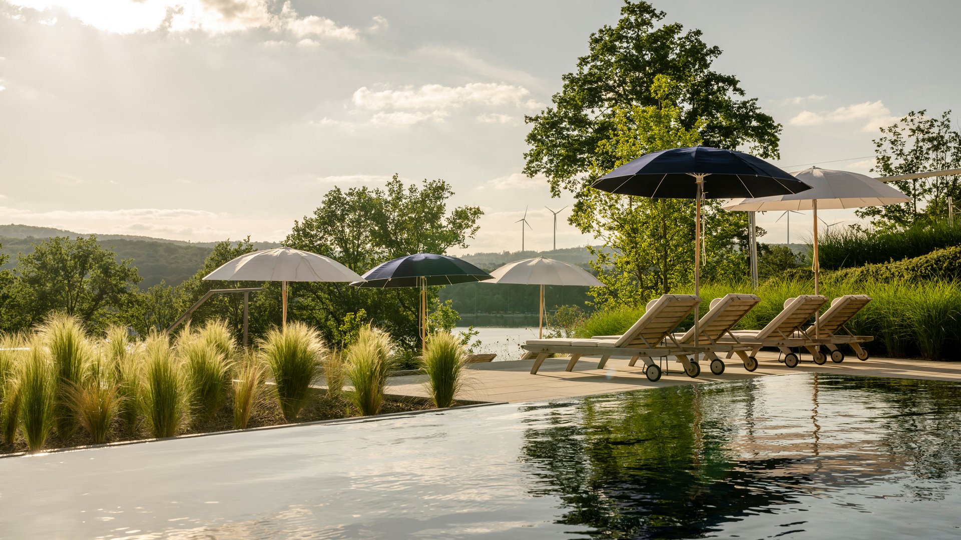 Seezeitlodge: Bildergalerie Pool mit Liegestühlen und Sonnenschirmen in natürlicher Landschaft bei Sonnenlicht