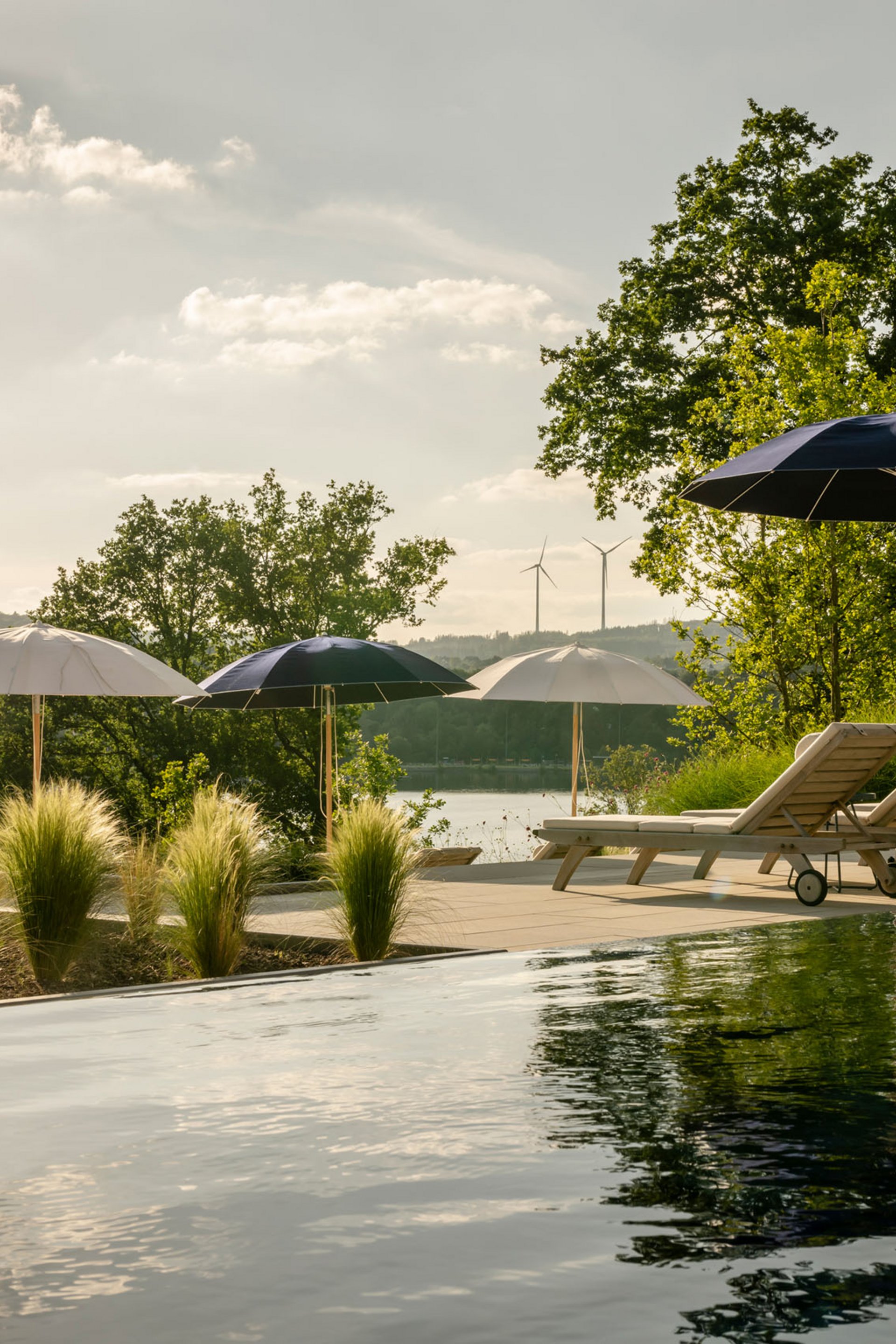 Seezeitlodge : Galerie photos Piscine avec chaises longues et parasols dans un paysage naturel sous la lumière du soleil