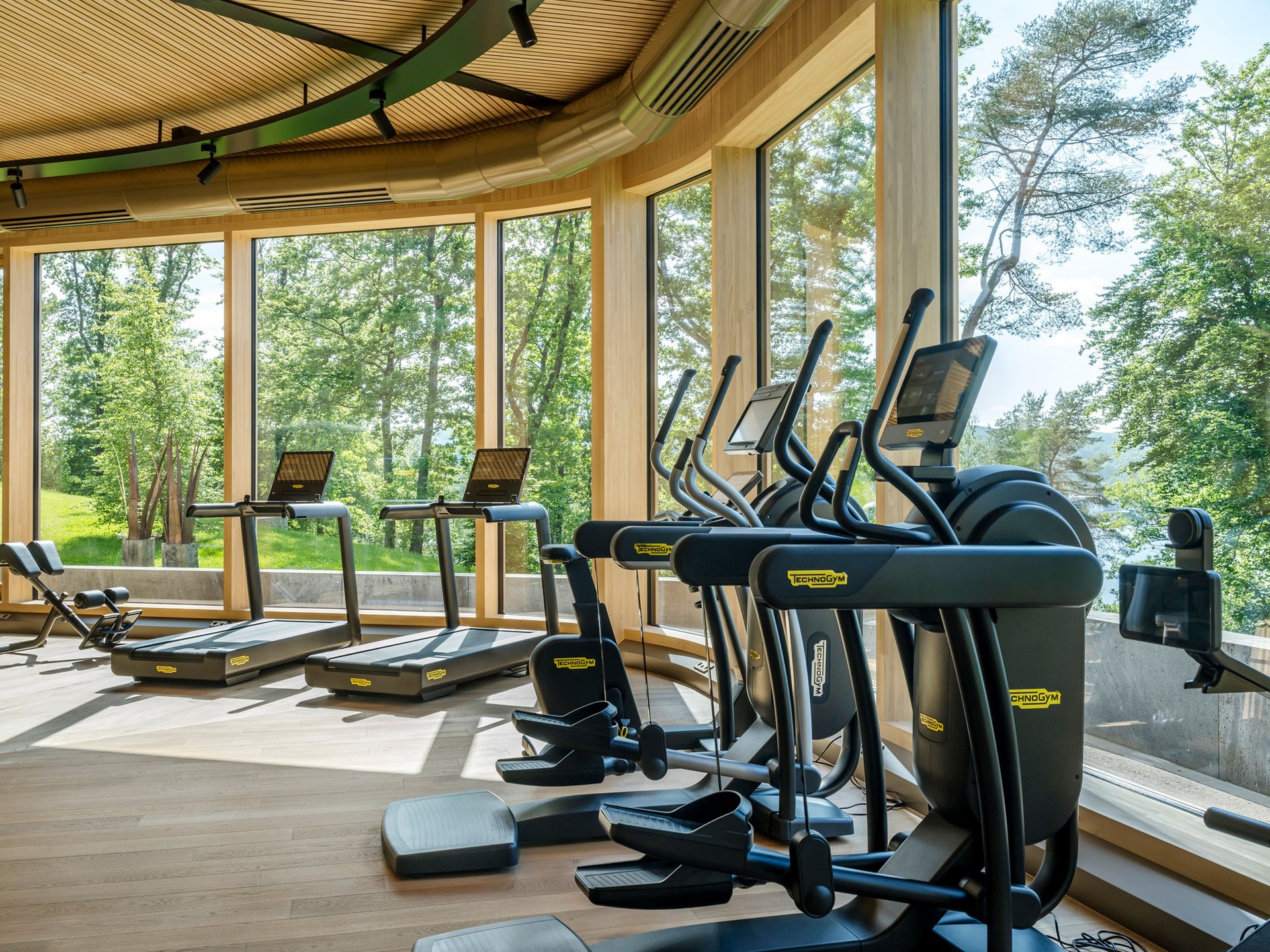 Ihr Wellnesshotel mit Yoga in Deutschland Fitnessraum mit moderner Ausrüstung und großen Fenstern mit Blick ins Grüne