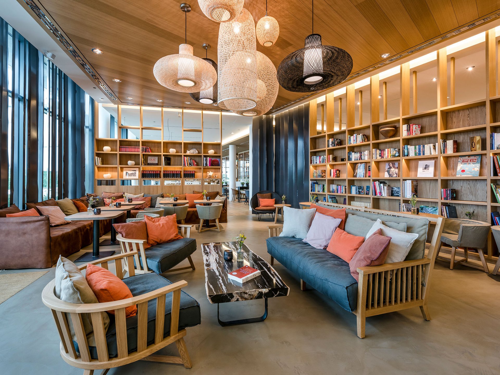 Seezeitlodge: Bildergalerie Moderne Bibliothek mit gemütlichen Sofas, Holzregalen und Hängelampen