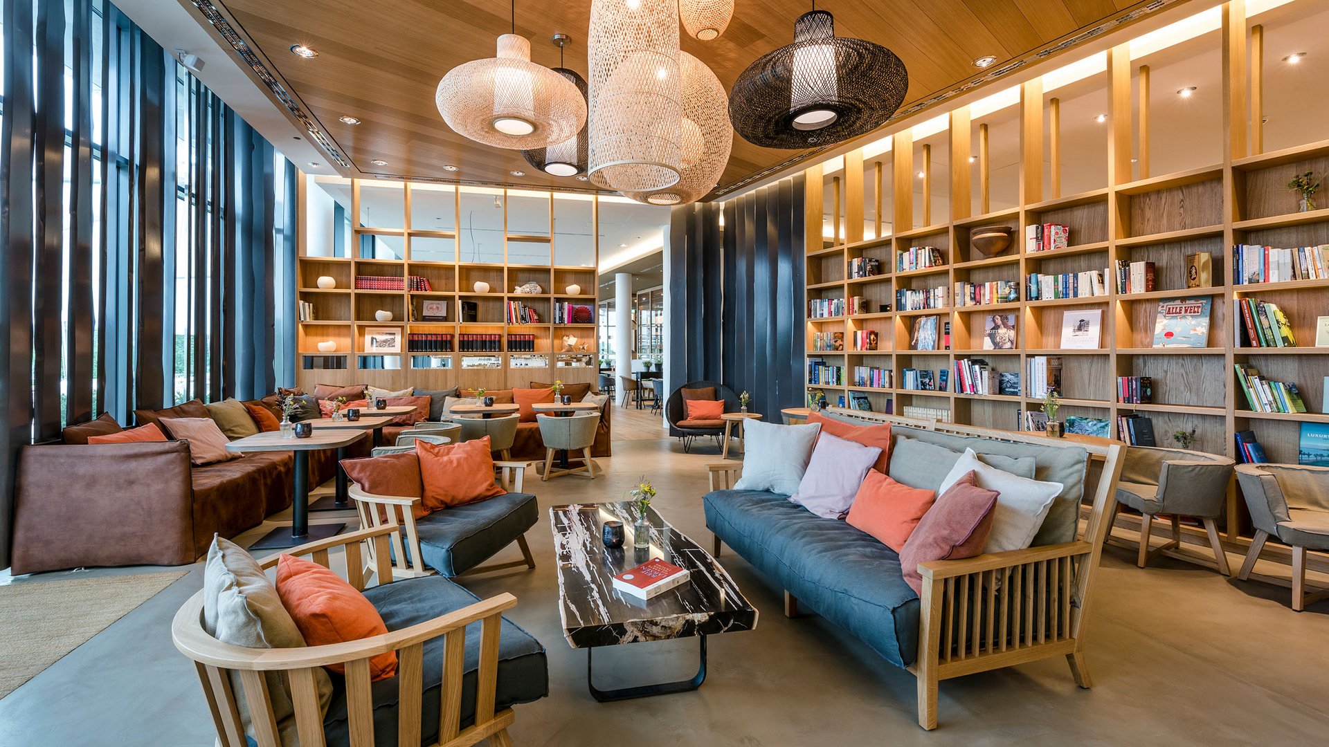 Seezeitlodge: Bildergalerie Moderne Bibliothek mit gemütlichen Sofas, Holzregalen und Hängelampen