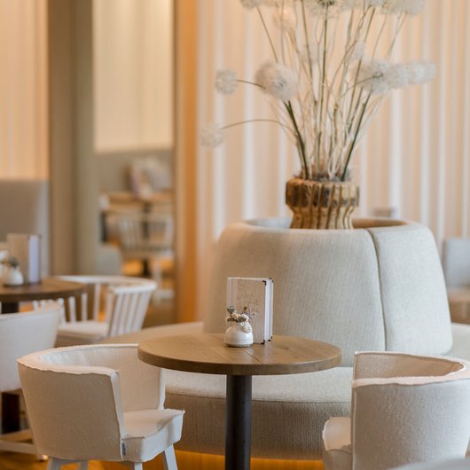 Seezeitlodge: Ihr Spa-Hotel am Bostalsee Gemütliche Sitzgruppe mit kleinem Holztisch und weißen Stühlen in elegantem Café