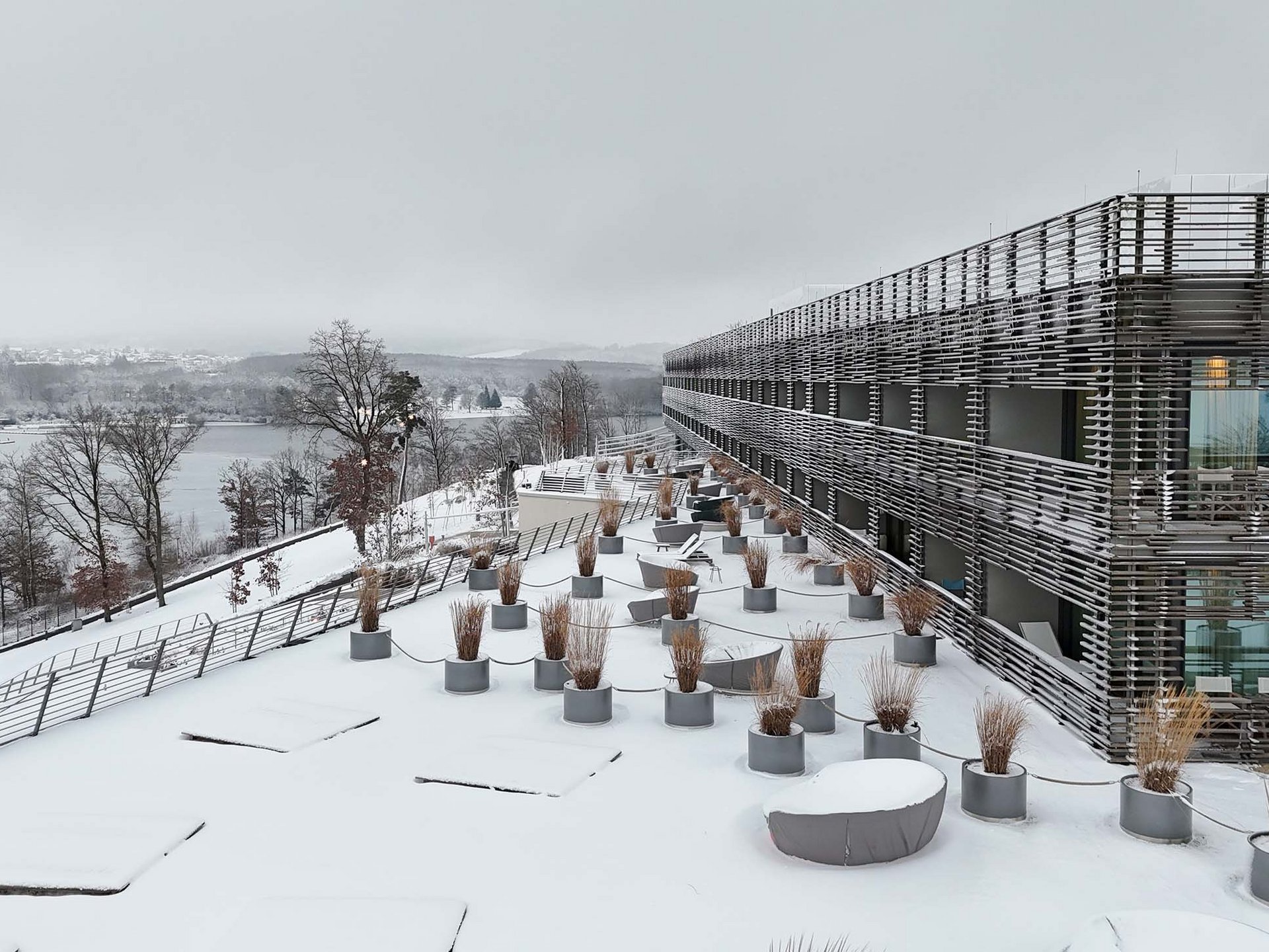 Die Seezeitlodge: Ihr Hotel am Bostalsee Verschneite Terrasse mit Pflanzkübeln neben einem modernen Gebäude und Blick auf eine winterliche Landschaft